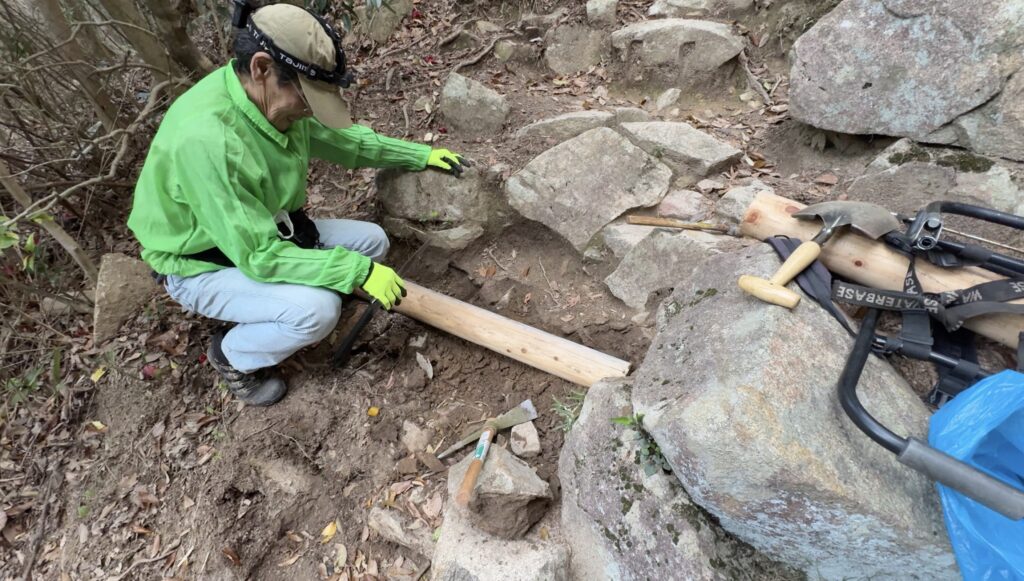 山道で丸太設置作業をする岡本学さん
