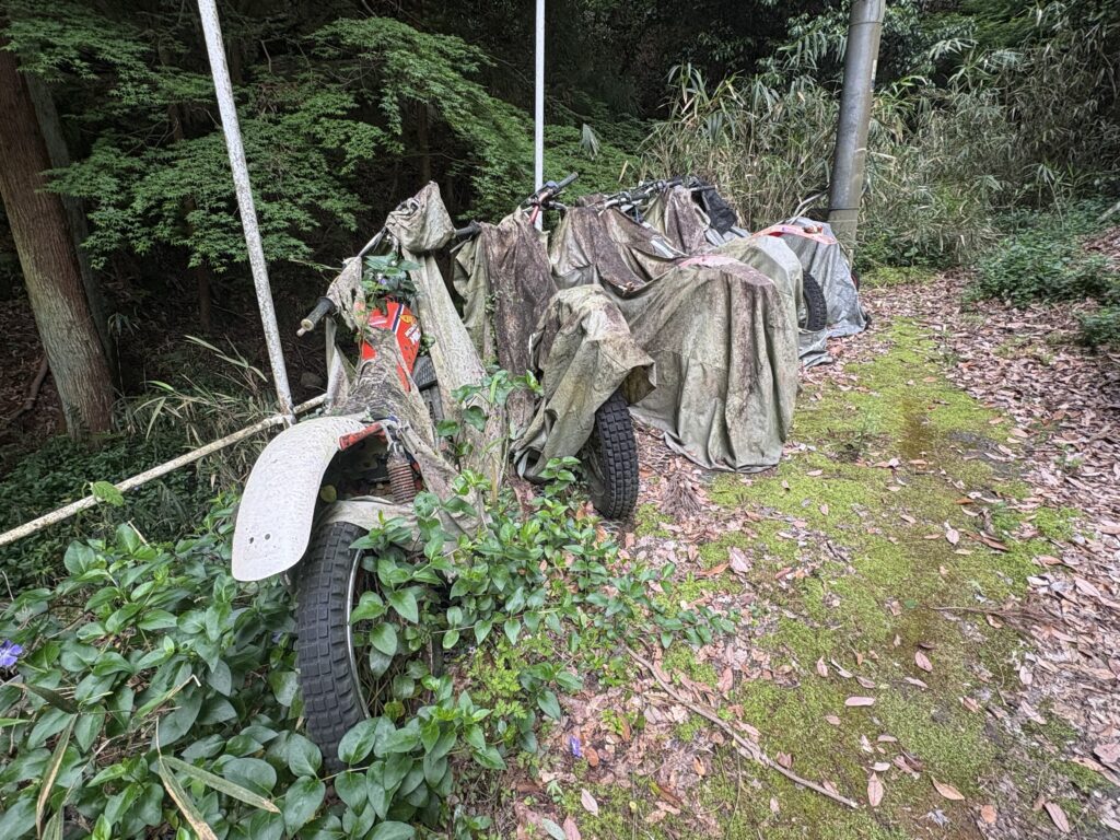 鉄板と丸太の橋の手前には廃車となったバイクが並ぶ。