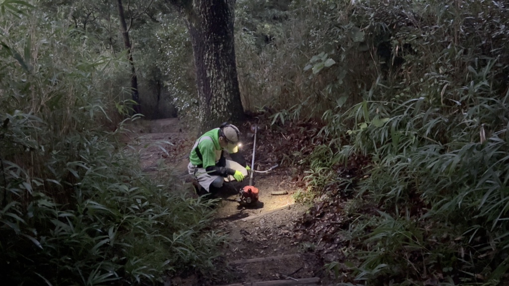 まだ暗い菊水山の登山道で、草刈機のスターターを引く様子